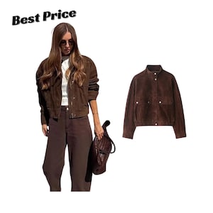 May include: A dark brown suede jacket featuring a high collar, a front zipper closure, and two front pockets with silver-toned snap buttons. The jacket has long sleeves and a straight hemline. The text Best Price is visible in the upper left corner.
