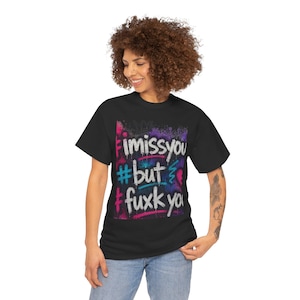May include: A black short-sleeve t-shirt featuring a central graphic with graffiti-style text that reads "i miss you #but #fuxk you" in white, surrounded by vibrant pink, blue, and purple spray paint splatters and abstract artistic markings.
