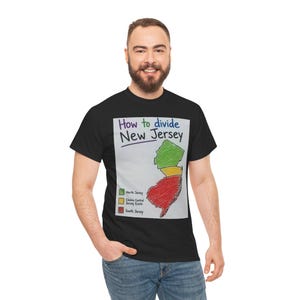 Può includere: Una t-shirt nera con una stampa grafica intitolata How to divide New Jersey. Il design mostra una mappa del New Jersey divisa in tre sezioni colorate: verde per il North Jersey, giallo per il Central Jersey e rosso per il South Jersey.
