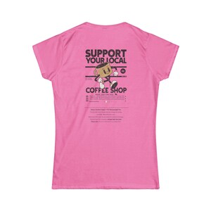 Può includere: Una t-shirt a maniche corte rosa acceso con una grafica nera sul retro. Il design include un personaggio a forma di tazza di caffè in stile cartoon con braccia e gambe, circondato dal testo SUPPORT YOUR LOCAL COFFEE SHOP e altri dettagli.