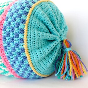 May include: A long, crocheted pillow with a colorful striped pattern and a turquoise blue crocheted top. The pillow has a long, colorful tassel.