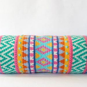 May include: A colorful crocheted bolster pillow with a geometric pattern in shades of blue, green, pink, orange, and yellow. The pillow has a fringe on each end.