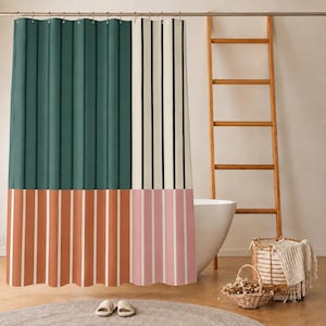 May include: A shower curtain featuring a color-blocked design with a large dark green panel on the left and a vertical striped section on the right. The bottom half displays alternating terracotta and white stripes, while the top right has thin black stripes on a cream background.