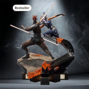 May include: A detailed statue featuring two characters in dynamic poses, wielding glowing lightsabers. One figure is clad in brown and black, the other in blue and white. The base has a fiery orange glow, with the word "Bestseller" in the corner.