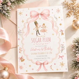May include: A rectangular birthday invitation card featuring a pink watercolor bow frame, a nutcracker and ballerina illustration, and text reading: Our Little Sugar Plum is turning one! Celestina's 1st Birthday, Saturday December 12 at 2pm.