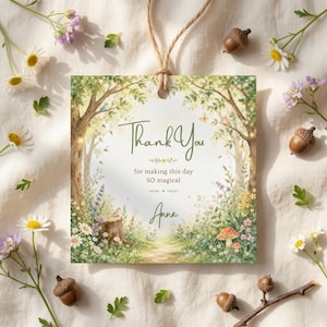 May include: A square tag with a watercolor illustration of a forest scene, featuring trees, flowers, and a path. The text "Thank You" is written in elegant script, with additional text below. A twine string is attached for hanging.