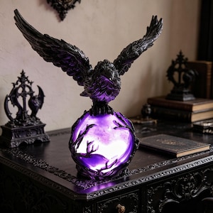 May include: A black raven sculpture with outstretched wings perched atop a glowing purple orb. The orb is encircled by dark branches, creating a gothic aesthetic. The sculpture is placed on a dark, ornate table, suggesting a decorative home accent.
