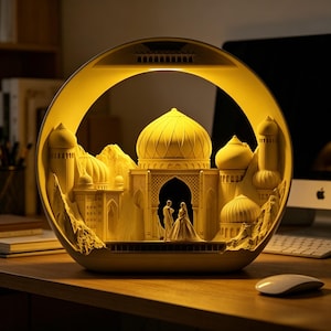 Peut inclure: Lampe décorative illuminée représentant un palais de style oriental avec des dômes et des arches. La lampe émet une lueur jaune chaleureuse et présente un couple sous une arche. La lampe est posée sur un bureau en bois. Environ 20 cm de diamètre.