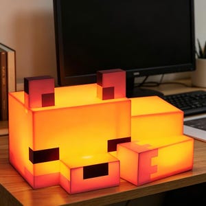 May include: A Minecraft-style fox lamp. The lamp is made of illuminated orange and red blocks, with black detailing for the eyes and nose. The design is reminiscent of a pixelated fox, suitable for a desk or bedside table.