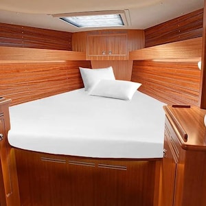 May include: A V-berth cabin interior featuring polished wood paneling on the walls and cabinetry. A bed with white bedding and two white pillows is positioned in the center. A rectangular skylight is set into the ceiling above the bed area.