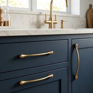 May include: Dark navy blue kitchen cabinetry featuring smooth, matte-finish gold metal drawer pulls and a vertical cabinet handle. The hardware has a slender, curved design with rounded ends, contrasting against the deep blue cabinet doors.