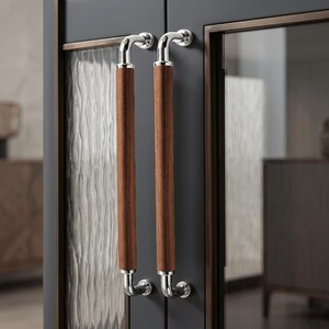 May include: Two vertical cabinet handles featuring cylindrical brown wood grips with polished chrome metal ends and mounting brackets, attached to dark grey cabinet doors with textured glass panels and bronze-toned metal trim frames.