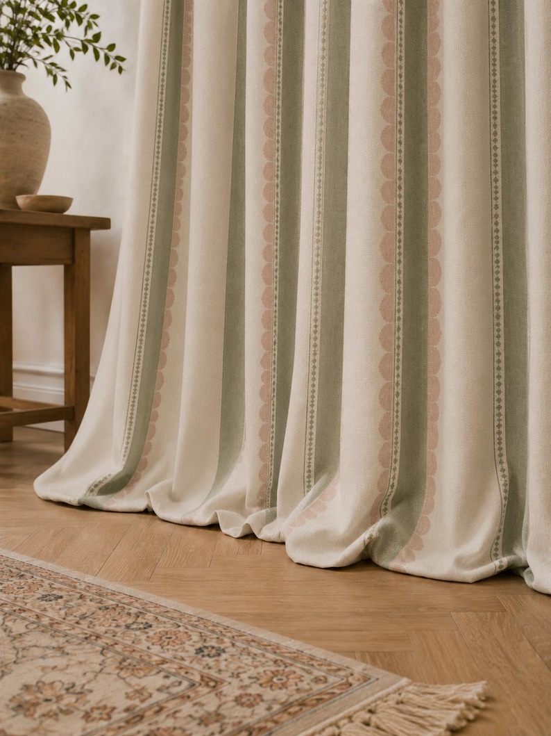 May include: A floor-length curtain featuring vertical stripes in cream, sage green, and soft pink. The fabric displays a repeating pattern of scalloped edges and thin geometric lines, creating a textured appearance with soft, cascading folds.