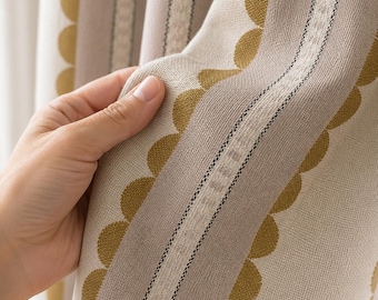 May include: A curtain panel featuring a vertical pattern of mustard yellow scalloped edges and beige stripes. The fabric has a textured weave with alternating bands of solid color and intricate linear detailing, creating a structured appearance.