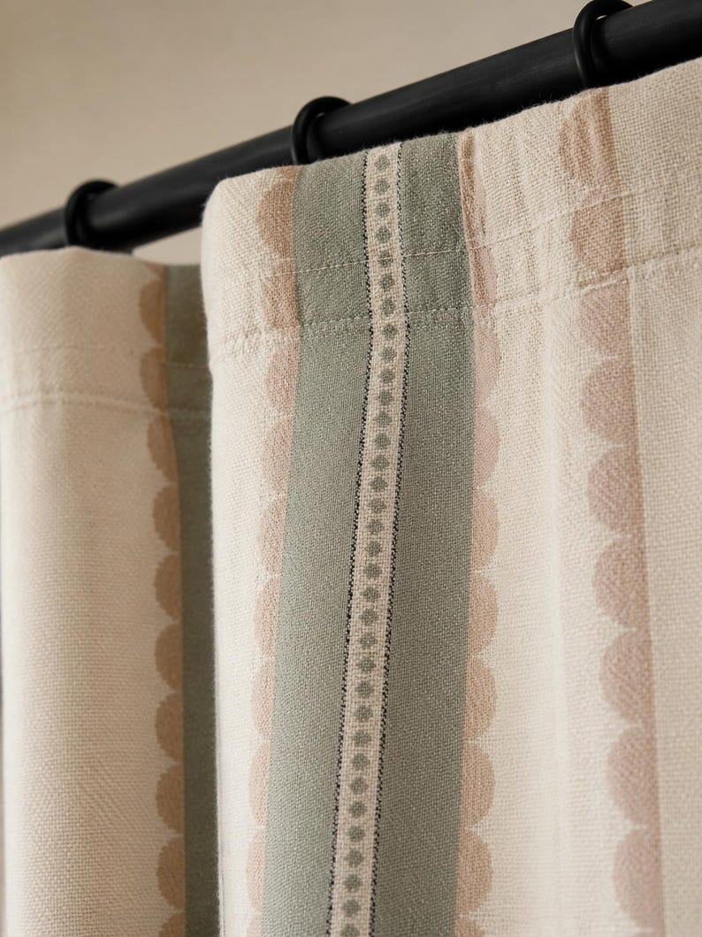 May include: A curtain panel hanging from a black rod with rings, featuring a cream-colored fabric with vertical stripes in sage green and soft beige. The design includes a central decorative band with a repeating diamond pattern and scalloped edges.