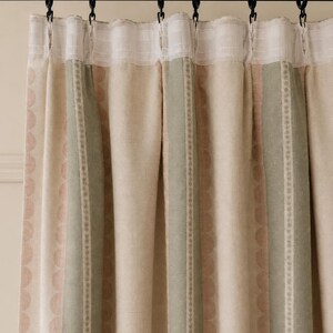 May include: A pleated curtain panel featuring vertical stripes in muted sage green, soft beige, and pale pink. The fabric displays a subtle scalloped pattern within the stripes and is suspended from a black rod by black metal curtain rings.