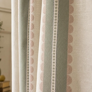 May include: A textured fabric curtain featuring vertical stripes in sage green and soft pink. The design includes a central sage green band with a delicate dotted line, flanked by scalloped pink edges on a cream-colored woven background.
