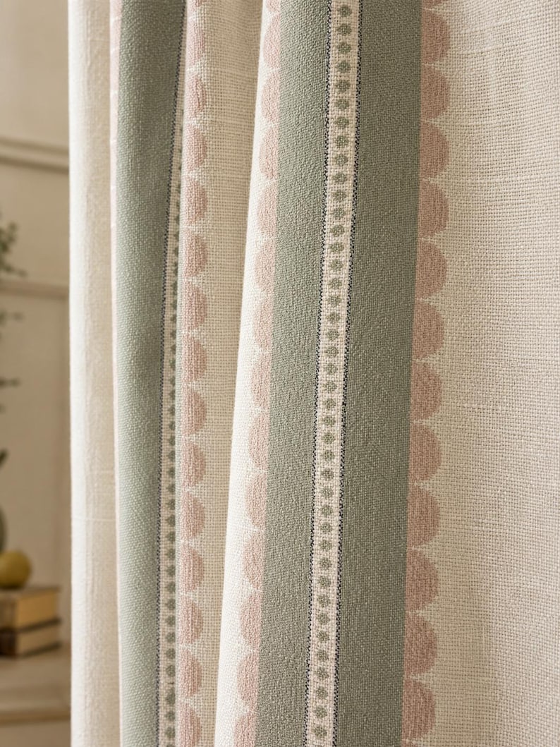 May include: A textured fabric curtain featuring vertical stripes in sage green and soft pink. The design includes a central sage green band with a delicate dotted line, flanked by scalloped pink edges on a cream-colored woven background.