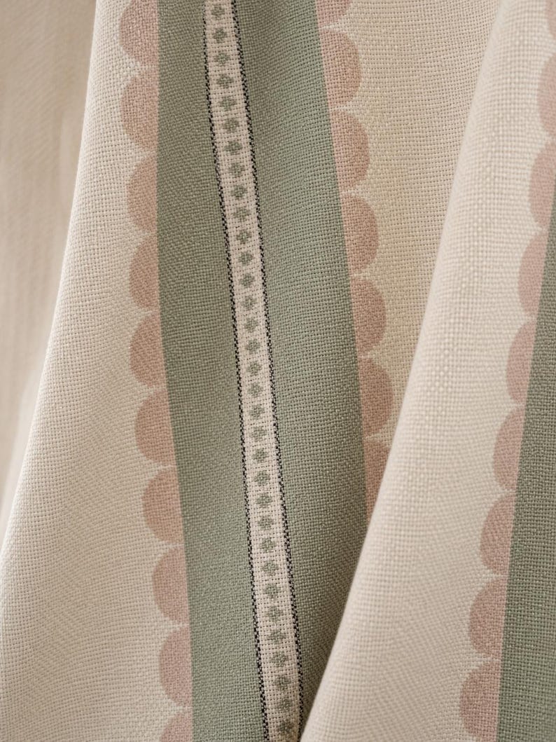 May include: A woven fabric featuring vertical stripes in sage green and cream, accented by rows of soft pink scalloped edges and a central decorative band containing a repeating geometric diamond pattern in green and black on a cream background.