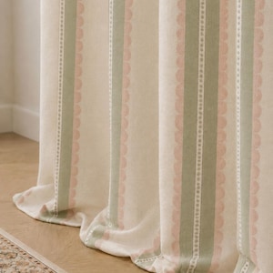 May include: A floor-length curtain featuring a vertical striped pattern in shades of sage green, soft pink, and cream. The fabric displays alternating bands of solid color and a delicate scalloped edge design, creating a textured appearance.