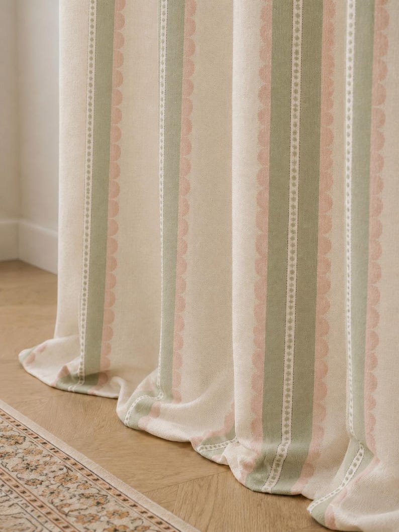 May include: A floor-length curtain featuring a vertical striped pattern in shades of sage green, soft pink, and cream. The fabric displays alternating bands of solid color and a delicate scalloped edge design, creating a textured appearance.