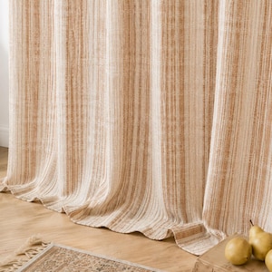 May include: A floor-length curtain featuring vertical stripes in shades of cream and tan. The fabric has a textured, woven appearance with subtle variations in color density throughout the vertical pattern, creating a soft, draped effect.