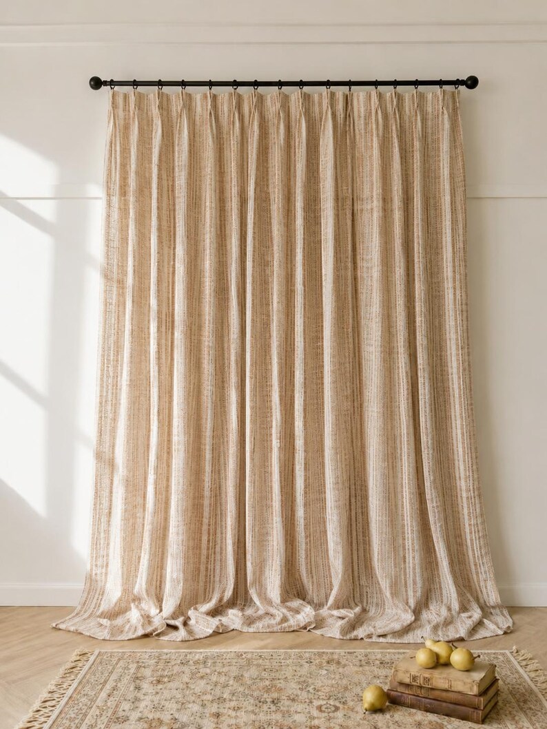 May include: A floor-length curtain with a vertical striped pattern in shades of beige and cream. The curtain features a pleated top header and is suspended from a black metal rod with rings. The fabric has a textured, woven appearance.