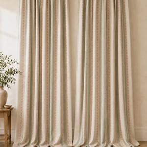 May include: Two floor-length curtains hanging from a black rod, featuring a vertical striped pattern in shades of cream, sage green, and muted pink. The fabric has a textured appearance with repeating geometric motifs along the stripes.