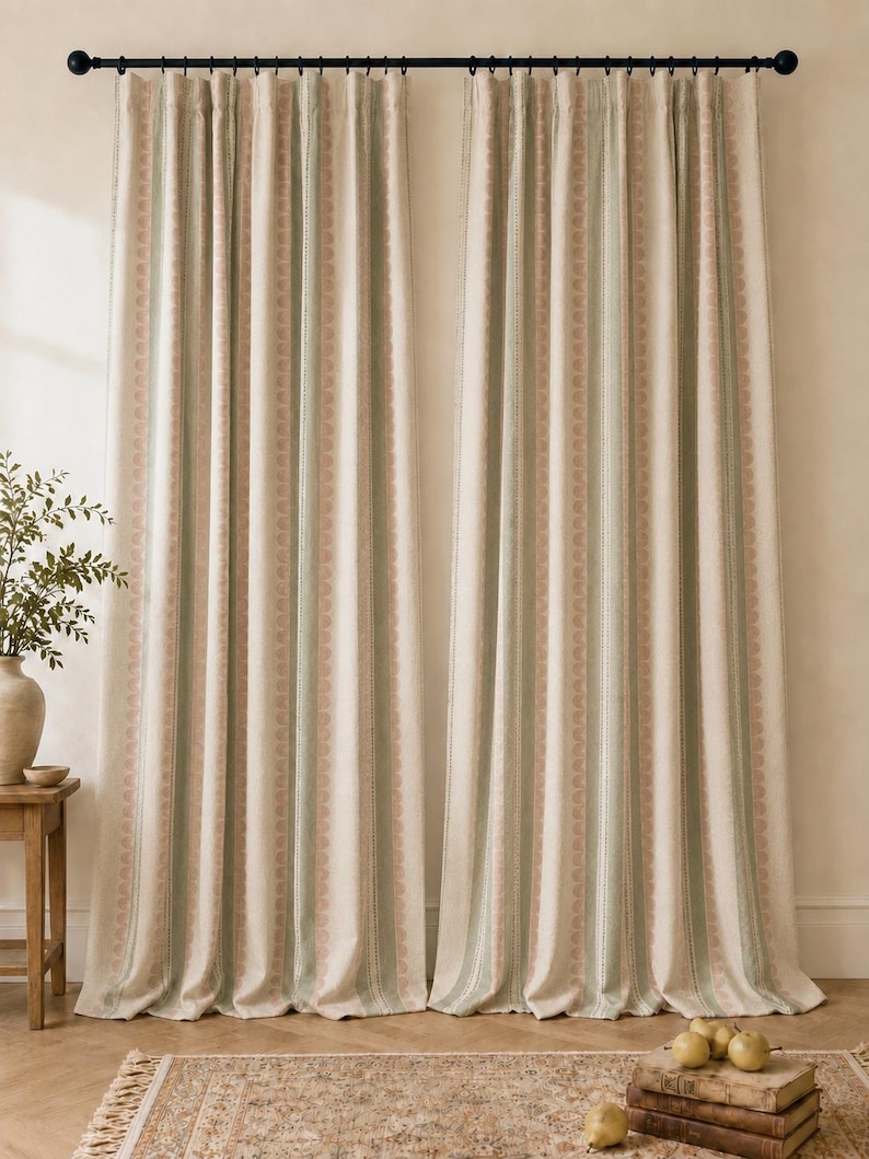 May include: Two floor-length curtains hanging from a black rod, featuring a vertical striped pattern in shades of cream, sage green, and muted pink. The fabric has a textured appearance with repeating geometric motifs along the stripes.