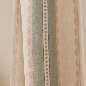 May include: A woven fabric featuring vertical stripes in sage green and beige. The pattern includes a central band with a small repeating diamond motif, flanked by wider sage green stripes and scalloped edges in a soft peach tone on a beige base.