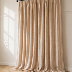 May include: Floor-length curtains featuring a vertical striped pattern in shades of beige and cream. The fabric has a textured appearance and hangs from a black metal curtain rod with circular rings, creating soft, uniform pleats along the length.