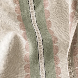 May include: A woven fabric featuring a cream-colored base with vertical stripes. A central sage green band is flanked by rows of soft pink scalloped circles. A narrow white and black geometric border runs through the center of the green stripe.