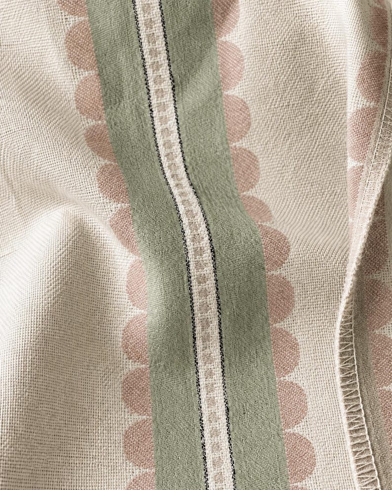 May include: A woven fabric featuring a cream-colored base with vertical stripes. A central sage green band is flanked by rows of soft pink scalloped circles. A narrow white and black geometric border runs through the center of the green stripe.