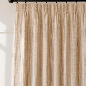 May include: A floor-length curtain panel featuring a vertical striped pattern in shades of tan, beige, and white. The fabric has a textured weave and is suspended from a black metal rod with matching black rings, creating uniform pinch pleats.