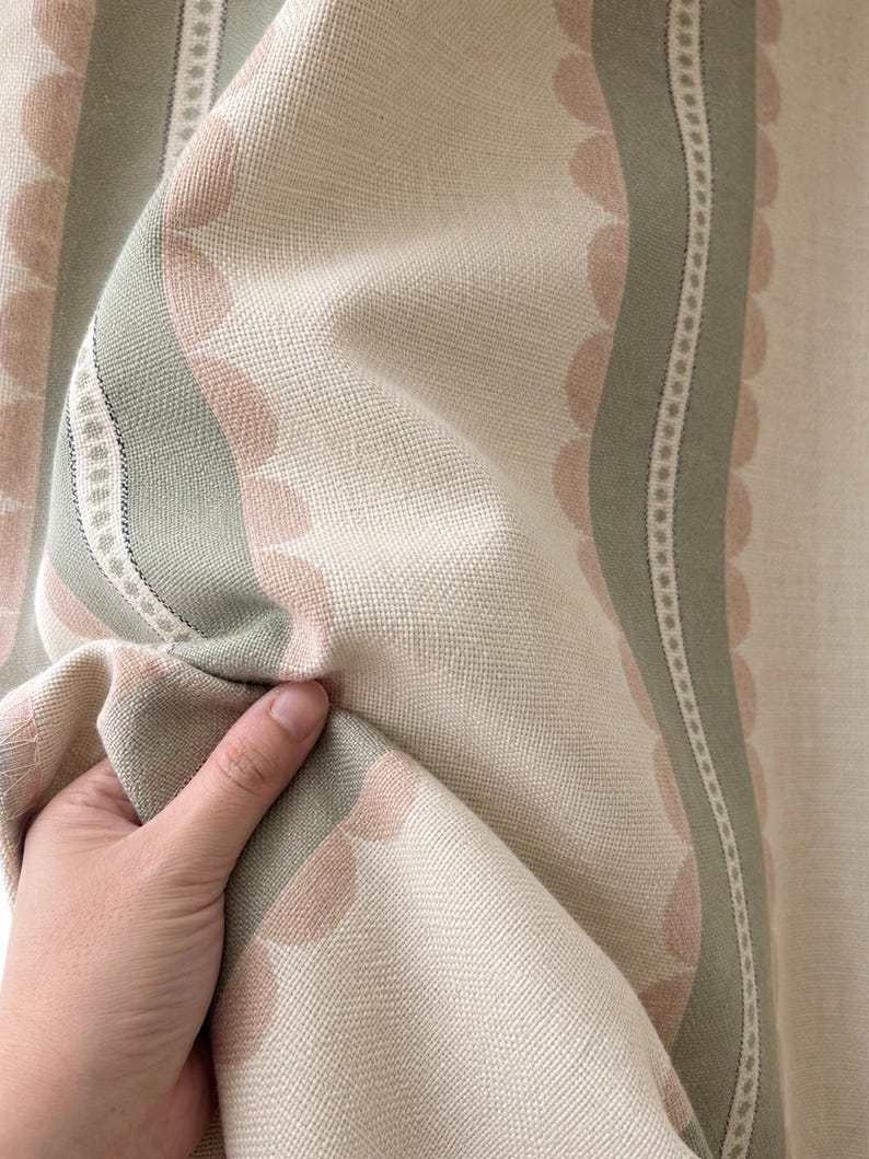 May include: A woven fabric featuring a pattern of vertical sage green and soft pink scalloped stripes. The design includes thin white lines with small dot details running between the colored bands, set against a cream-colored background.