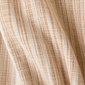 May include: A woven fabric featuring a vertical striped pattern in shades of tan and off-white. The material displays a textured, slubbed appearance with visible fibers running in parallel lines, creating a consistent, repeating linear design throughout.