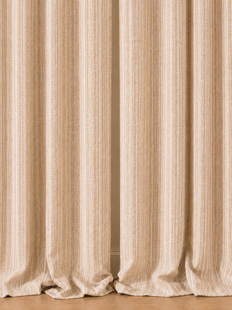 May include: A pair of floor-length curtains featuring a vertical striped pattern in shades of beige, tan, and cream. The fabric has a textured, woven appearance with consistent pleats running from the top to the bottom hem of the panels.