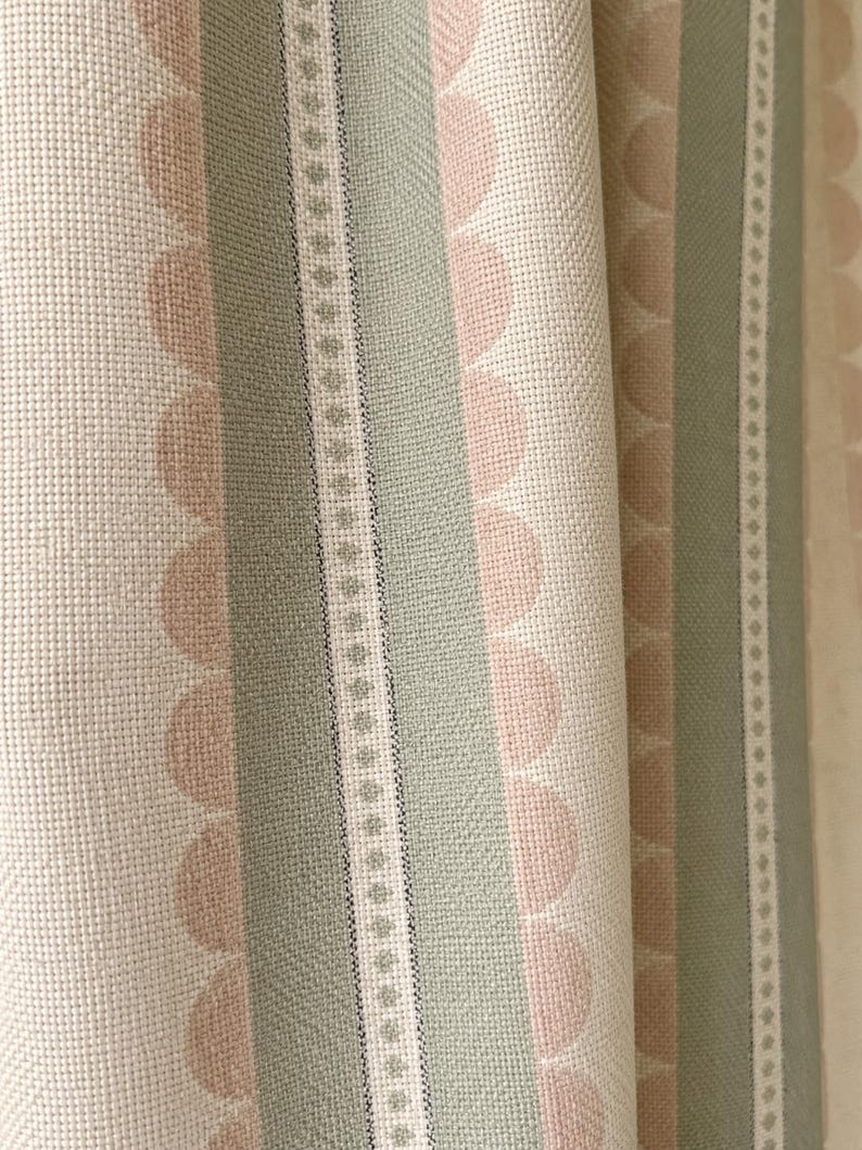 May include: A woven fabric featuring vertical stripes in sage green and soft peach. The pattern includes rows of scalloped semi-circles in peach alongside solid sage green bands and a narrow white stripe with a repeating small diamond motif.