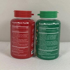 May include: Two supplement bottles with red and green lids. The red bottle has a label with supplement facts and ingredients, including fruit blends. The green bottle also has supplement facts and ingredients, including vegetable blends.