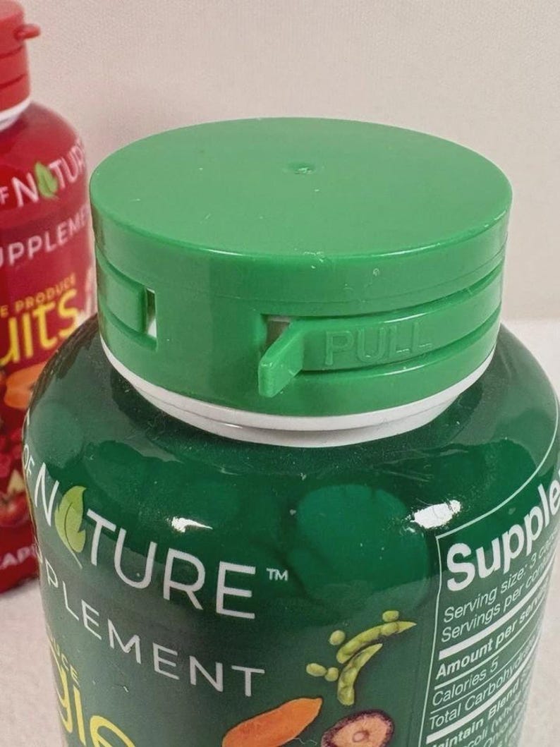 May include: Close-up of a green supplement bottle with a green cap. The cap has a "PULL" tab. The bottle is labelled "Nature Supplement" and contains a blend of fruits and vegetables.