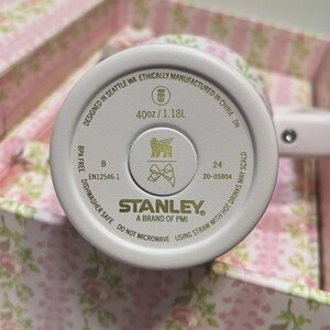 Op de afbeelding: Een close-up van de bodem van een witte Stanley-beker. De basis bevat de tekst "40oz / 1.18L", "Dishwasher Safe" en "BPA Free". Het Stanley-logo staat in het midden.