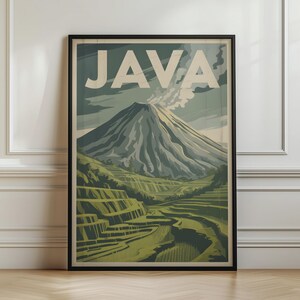 May include: A framed vertical poster featuring a stylized illustration of a volcano with smoke rising from the peak. The word JAVA is printed in large, bold, cream-colored letters at the top. Below the volcano are green terraced rice fields.