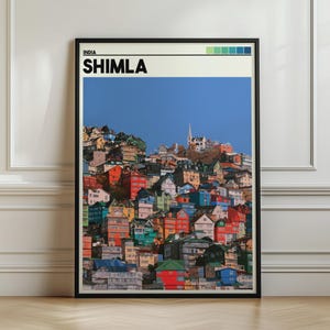 May include: A framed vertical wall art print featuring a photograph of the hillside city of Shimla, India. The image displays a dense cluster of colourful buildings in shades of red, blue, and green under a clear blue sky. The text reads INDIA SHIMLA.