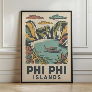 May include: A framed travel poster featuring a stylised illustration of the Phi Phi Islands. The artwork depicts a long-tail boat on calm water surrounded by limestone cliffs, foliage, and clouds in muted tones. The text PHI PHI ISLANDS is at the bottom.