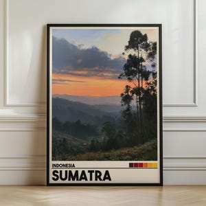 Op de afbeelding: Een ingelijste reisposter met een zonsondergang boven de bergen van Sumatra, Indonesië. De afbeelding toont een levendige oranje en blauwe lucht boven heuvels en hoge bomen. De tekst luidt INDONESIA SUMATRA met een kleurenpaletbalk eronder.
