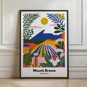 Pode incluir: Uma impressão artística emoldurada apresentando uma paisagem estilizada do Monte Bromo, na Indonésia. A ilustração gráfica exibe um pico de montanha azul-escuro sob um sol amarelo, rodeado por folhagem tropical colorida, flores e terreno abstrato.