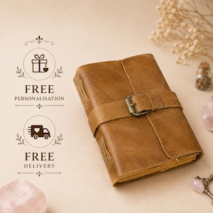 Puede incluir: Un diario de cuero marrón con una correa envolvente y un cierre de hebilla metálica. El diario tiene costuras laterales visibles y bordes de papel texturizados. El texto a la izquierda dice FREE PERSONALISATION y FREE DELIVERY con iconos.