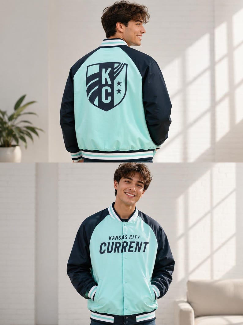 May include: A light blue and navy blue varsity jacket with the text "KANSAS CITY CURRENT" printed on the front. The back of the jacket features a shield design with the letters "KC" and two stars. The jacket has white and navy blue striped trim.