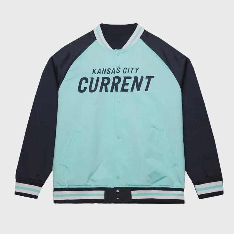 May include: A teal and navy blue varsity jacket with the text "KANSAS CITY CURRENT" in white. The jacket has a button-up front, side pockets, and striped detailing on the collar, cuffs, and hem.