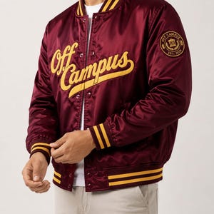 May include: Burgundy satin bomber jacket with yellow accents. The jacket features the text "Off Campus" in yellow script across the chest and a circular patch on the upper arm. The jacket has yellow stripes on the collar, cuffs, and hem.